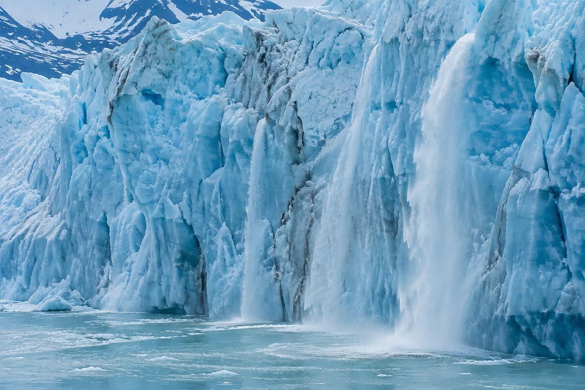 A blue glacier ice wall with meltwater pouring into the sea